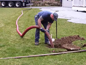Septic pumping technician servicing a residential septic tank with a vacuum hose in Newton, MA